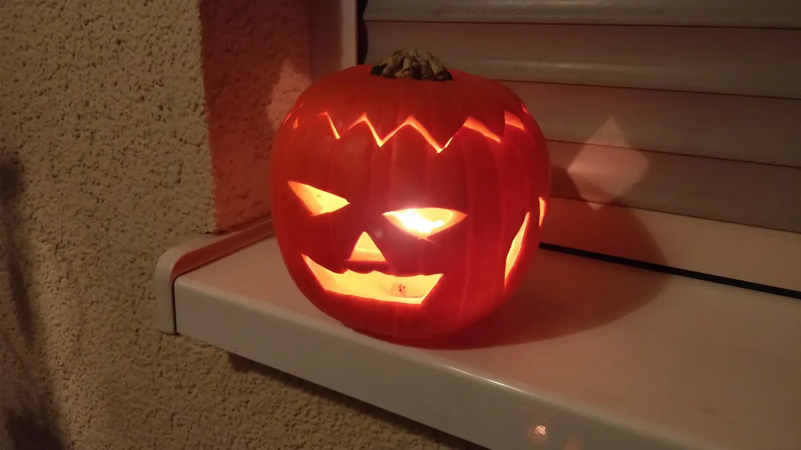 En karvad pumpalykta med trekantiga ögon och sicksackmönster runt locket lyser på en fönsterbräda en mörk kväll.