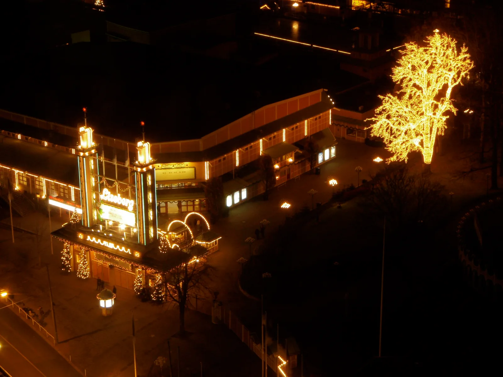 Lisebergs entré med julbelysning en decemberkväll, med ett träd fullt av ljus bredvid, sett uppifrån.