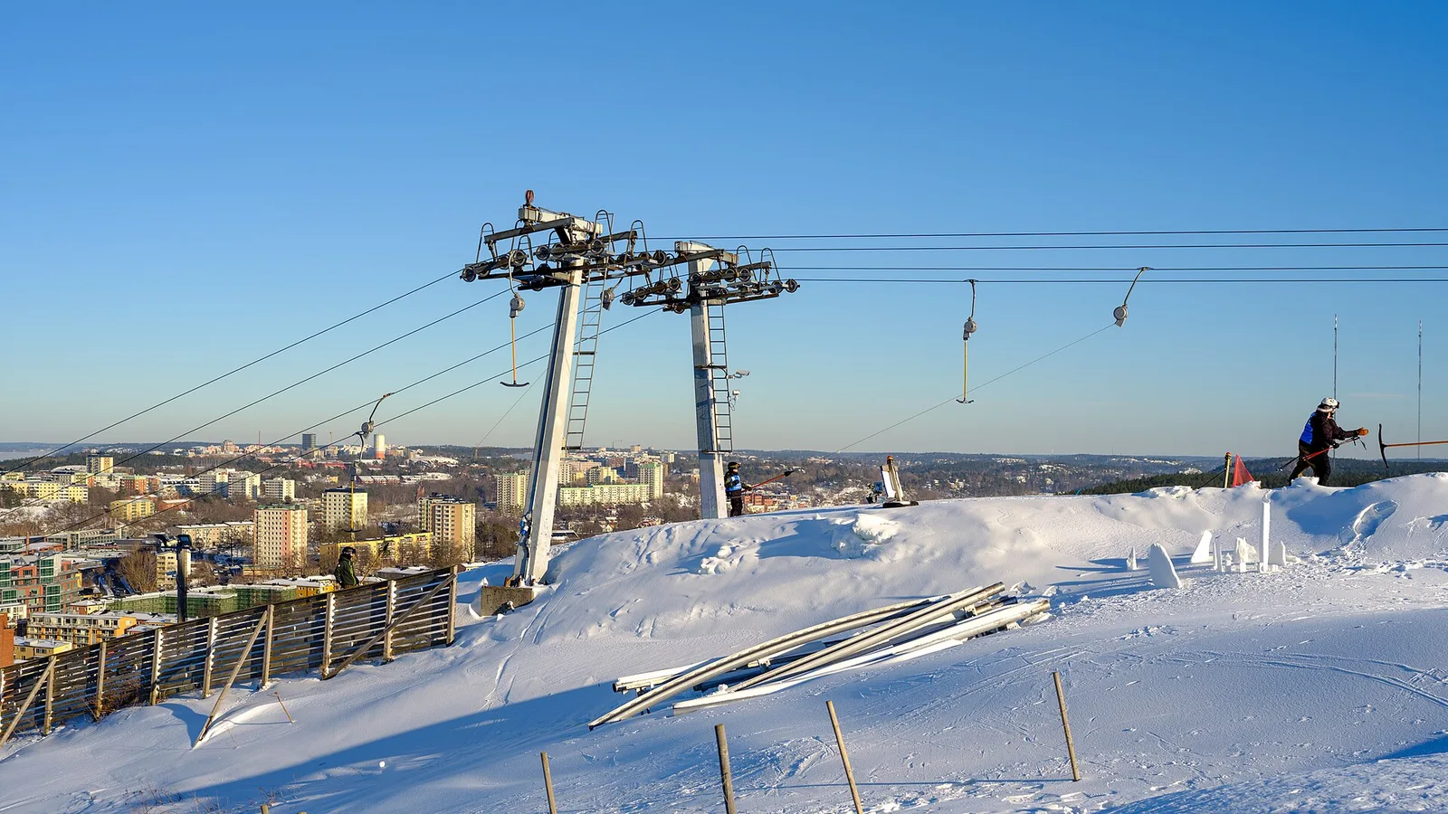 Liftstolparna på toppen av Hammarbybacken i snö och sol, med Stockholms bebyggelse nedanför.
