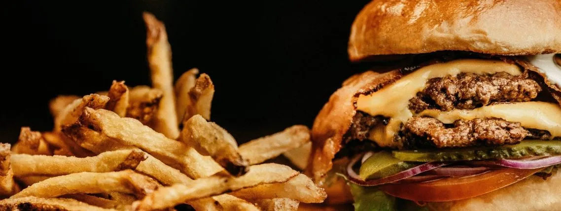 Sulīgs burgers ar sieru, dārzeņiem un frī kartupeļiem.