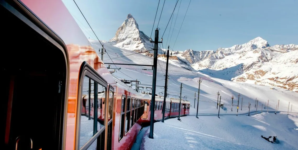 Trein in besneeuwde bergen met een heldere blauwe lucht op de achtergrond.