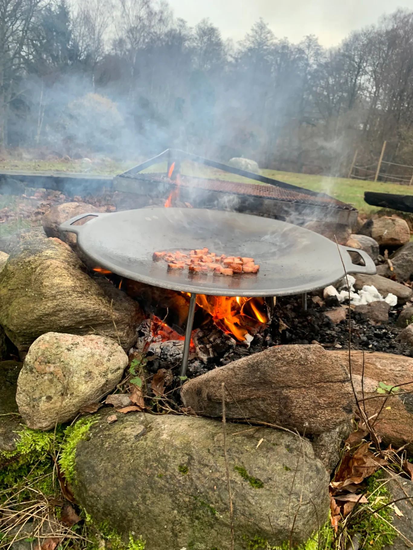 Ugunskura vieta ar lielu pannu un desiņām, kas grilētas uz atklātas uguns.