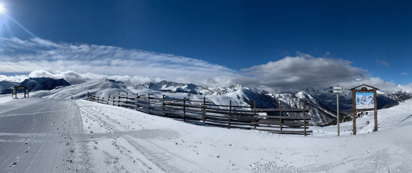 Winterlandschaft mit verschneiten Alpenbergen und einem klaren blauen Himmel, einer frisch präparierten Skipiste im Vordergrund.