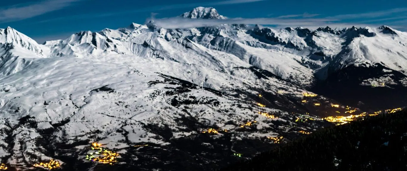 Besneeuwde bergen met een verre piek en een verlichte vallei bij de schemering.