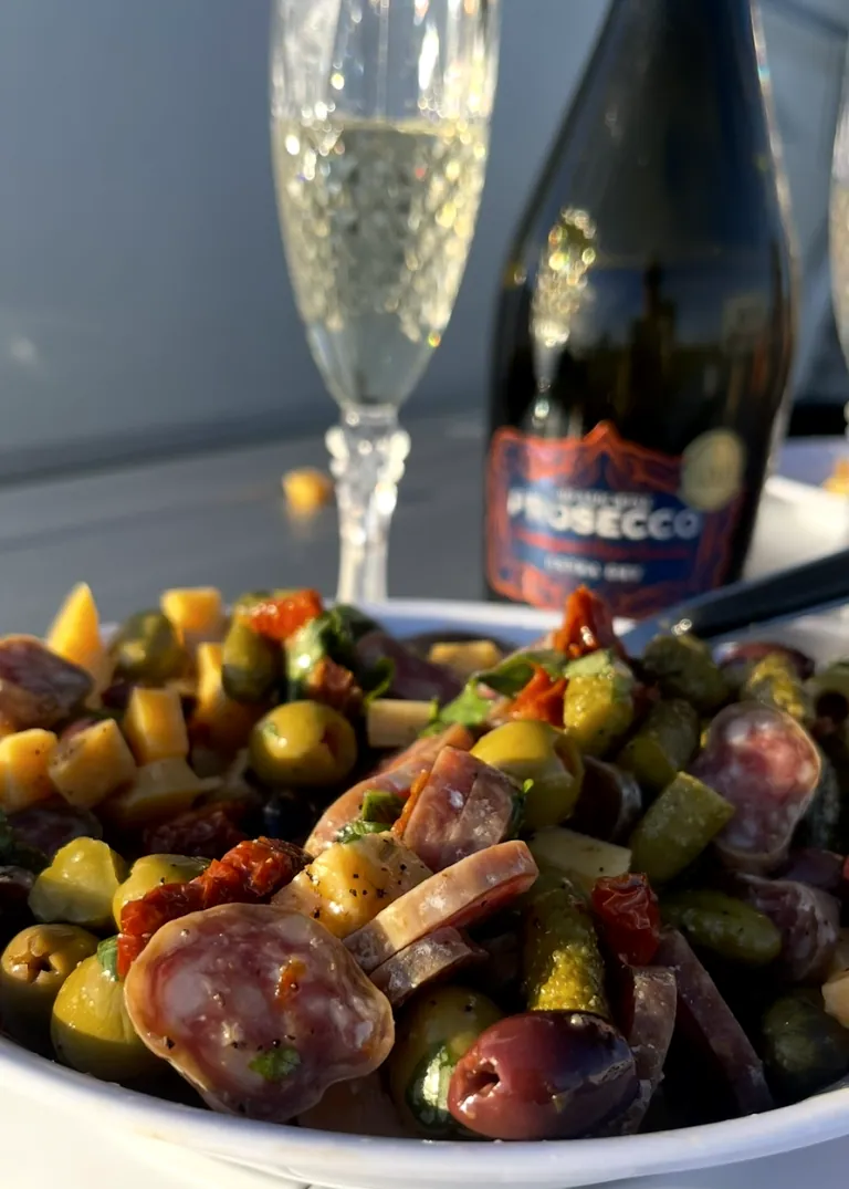Kaussi marineeritud oliivid ja charcuterie, šampanja pudel taustal.