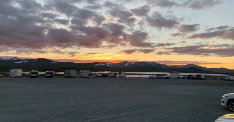 Zonsondergang over de bergen met donkere wolken en geparkeerde auto's op de voorgrond. De oude mijn op de achtergrond.