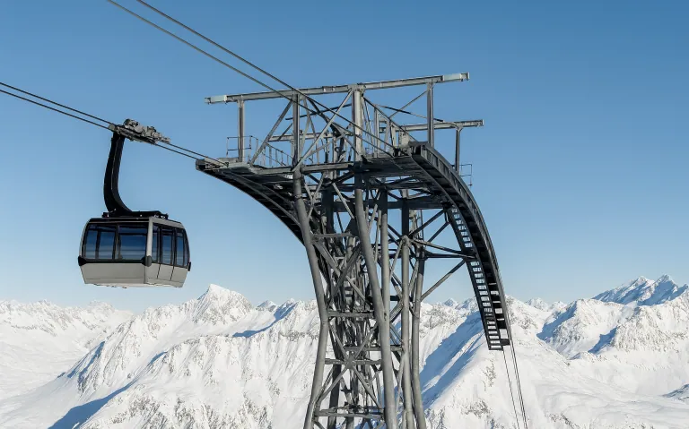 Stollift med gondol som svävar över snötäckta fjäll.