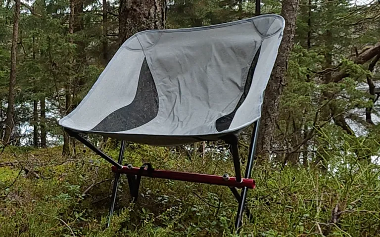 Sulankstoma, pilka ultralengva stovyklavimo kėdė miško aplinkoje.