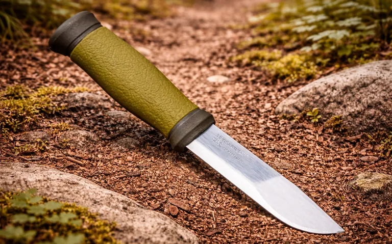 Foldekniv med grønt håndtak liggende på en smal sti omgitt av mose.