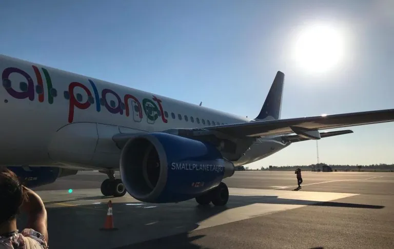 Lėktuvas su tekstu visa planeta“ stovi oro uoste po saulėtu dangumi.