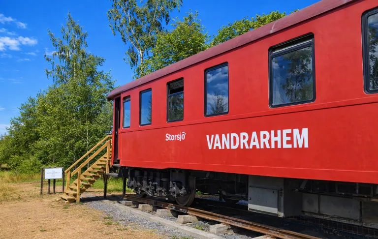 Punane rongivagun tekstiga "Vandrarhem" (hostel), mida ümbritsevad rohelus ja selge sinine taevas.