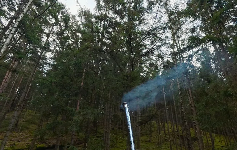 En foss renner ned mellom tett skog med grønt og tåke.