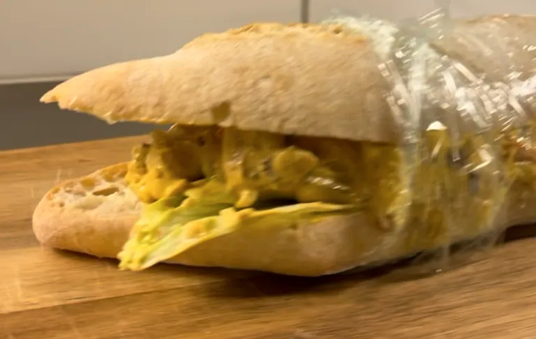 En sandwich fyldt med kylling og sauce, indpakket i plastfilm.
