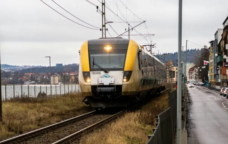 Koltåg närmar sig längs en spårvidd nära en väg och vattnet. Wetter grå himmel.