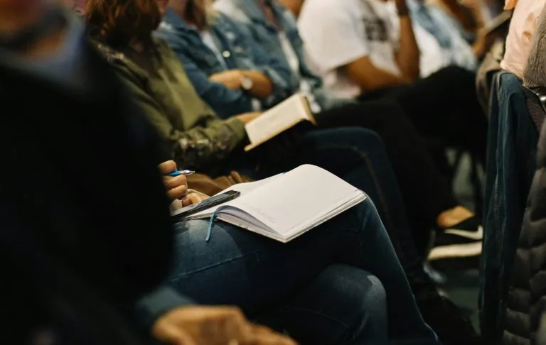 Mehrere Leute sitzen in einem Konferenzraum und schreiben in Notizblöcken.