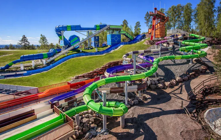 Waterglijbanen in een pretpark met verschillende kleurrijke bochten en weelderige omgeving.
