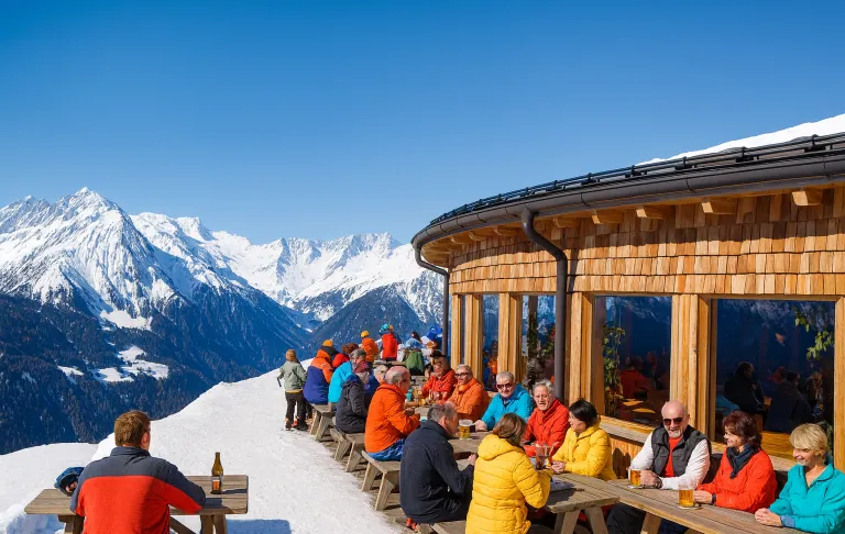 Illustration of people sitting at an outdoor café in the mountains with snow-covered mountains behind.