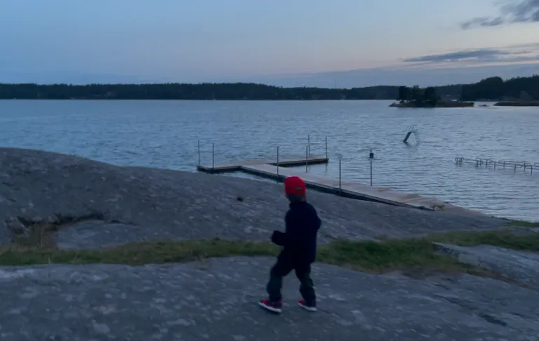 En dreng i en rød hat går på klipper ved en sø i skumringen.