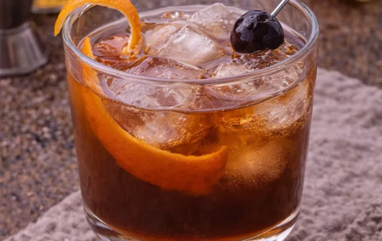 Ett glas med drink, isbitar, apelsinskal och ett körsbär på ett cocktailspett.