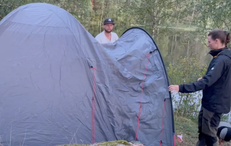 Twee mensen staan bij een tent opening in een bos gebied.