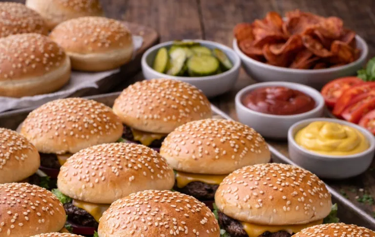 Sesame bun with hamburger, pickles, bacon, and sauces on a wooden surface.
