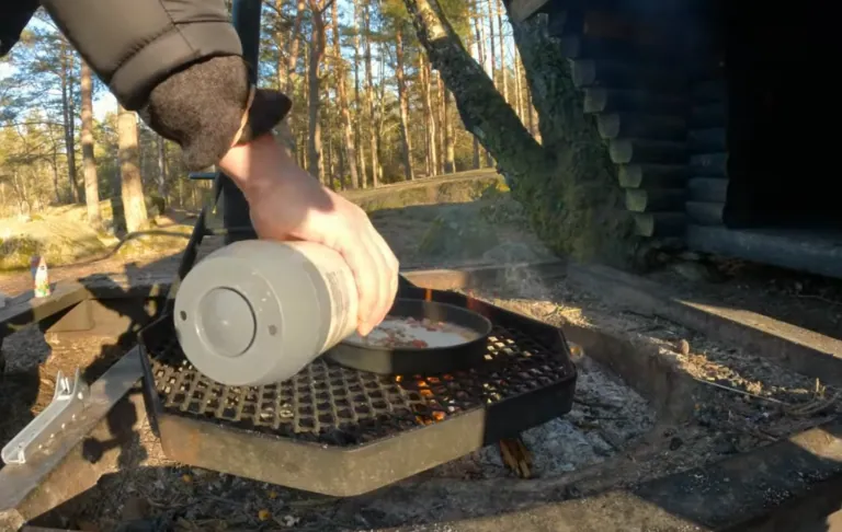 Roku ielej kolbule mīklu no krūze pār grilētu zivis mežā.