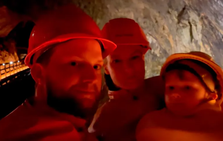 Drie mensen in helmen, een volwassene en een kind, poserend in een grot met rode verlichting.