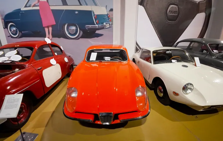 Drei Oldtimer: ein roter Sportwagen, zwei ältere Modelle im Hintergrund.