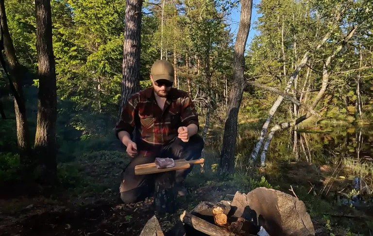 Een man die kookt over een open vuur in het bos, omgeven door bomen en de natuur.