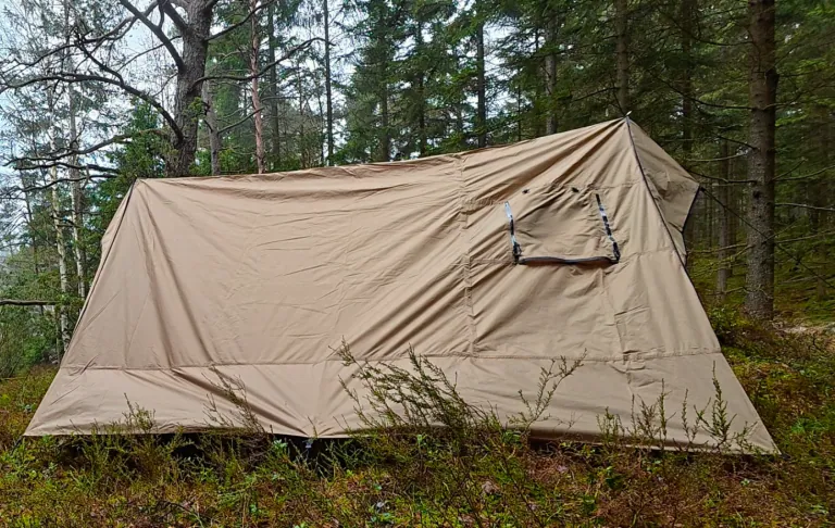 Een lichtbruine tent in een bos met bomen op de achtergrond.
