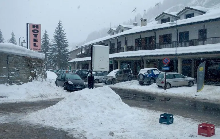 Snow-covered hotel area with cars and snowdrifts on the street.