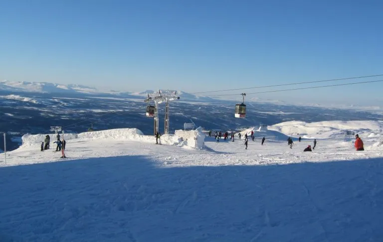 Ski slope with lifts and skiers on snow-covered terrain under a blue sky.