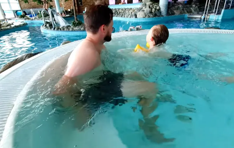 En voksen og et barn leger i en pool med klart, blåt vand.