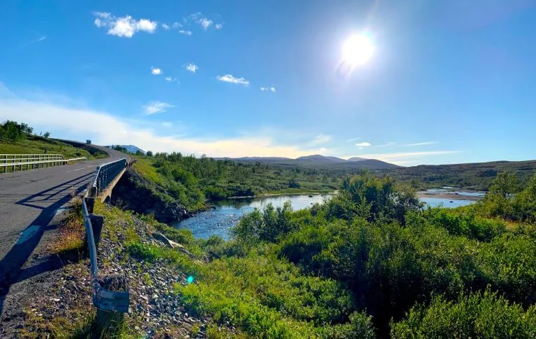 Berglandschap met brug over Saxån op Stekenjokk, groene planten en een zonnige hemel.