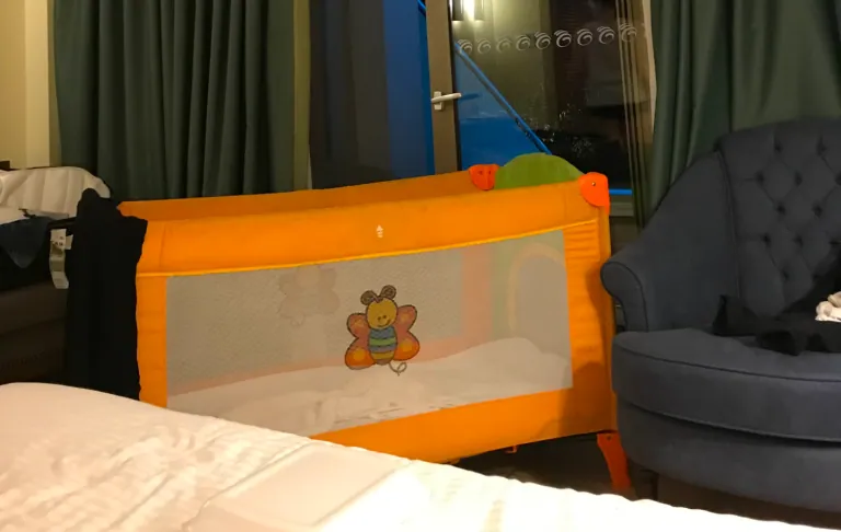 Een oranje kinderbed met een mesh paneel en speelgoed motieven, geplaatst in een kamer.
