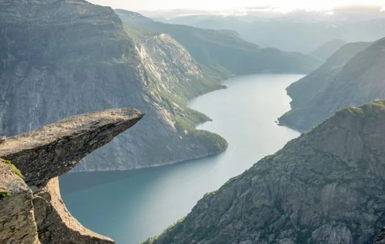 Vaizdas per fjordą su stačiomis uolomis ir ramiu vandeniu.