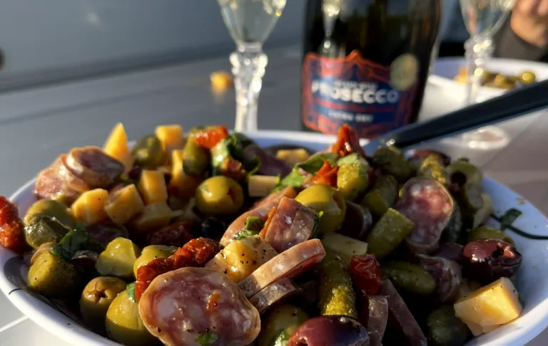 Tallrik med sallad av oliver, chorizo och grönsaker, med ett glas prosecco i bakgrunden.