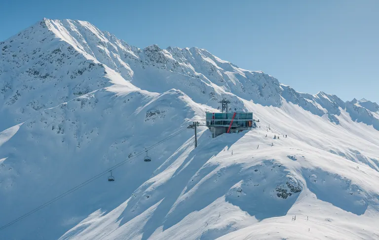 Illustration of snow-covered mountains with a ski lift stretching upward in clear weather.