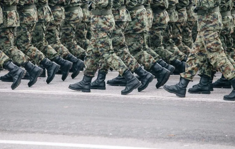 Karavīri maskēšanās uniformās soļo soli melnā zābaki.