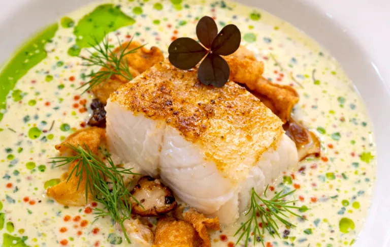 Stekt fiskfilé med krämig sås, svamp och örter, dekorerad med klöverblad.