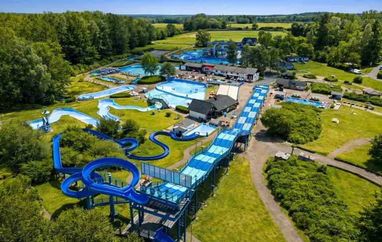 Een uitzicht op een waterpark met glijbanen en zwembaden omgeven door groen.