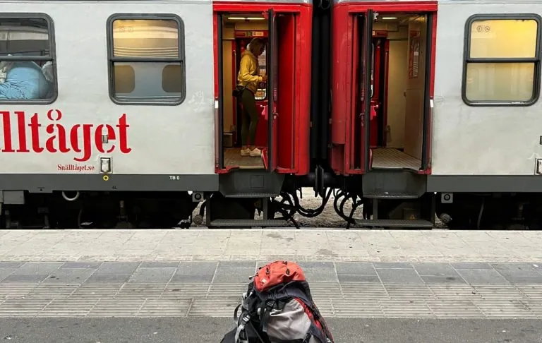 Seljakotiga mees seisab rongiplatvormil avatud rongi ees.