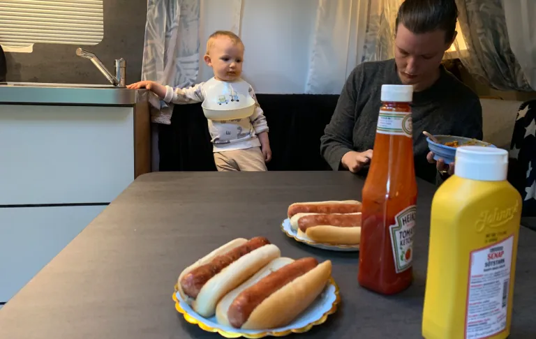 En voksen og et barn sidder ved et bord med hotdogs og sider.
