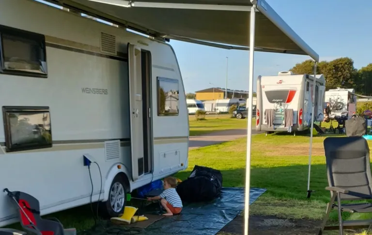 En campingvogn med fortelt, et barn leger på gulvet og andre campingvogne i baggrunden.