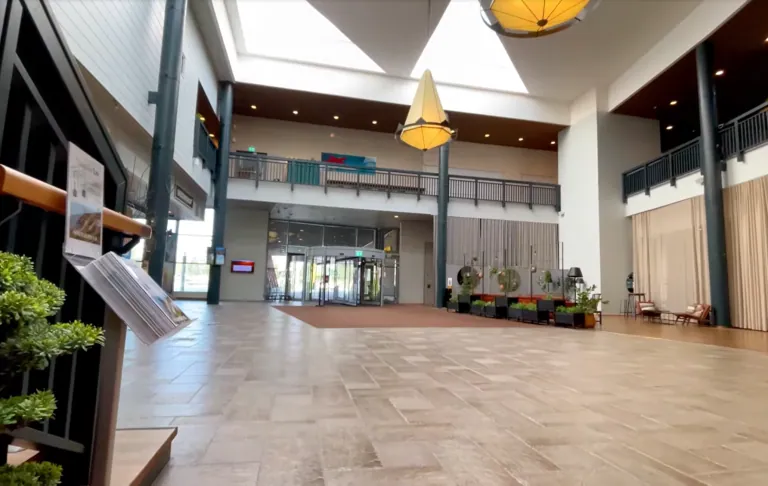 Een lichte, luchtige kamer met een hoog plafond, planten en een ingang op de achtergrond.