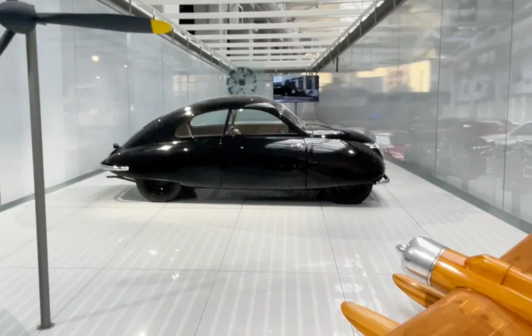 Ein schwarzes Auto in einer modernen Ausstellungshalle mit weißem Boden und Glaswänden.