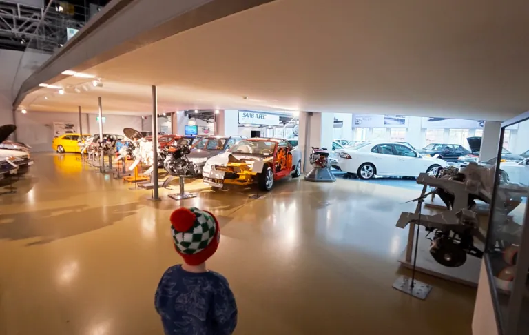 Kind steht vor einer Ausstellung von verschiedenen Autos in einem Automuseum.