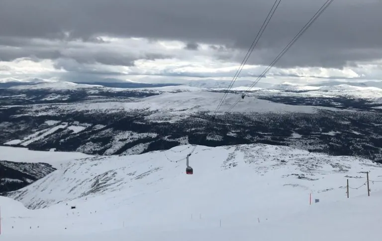 Utsikt över snöklädda fjäll och åres kabinbana/gondolbana under ett molnigt himmel.