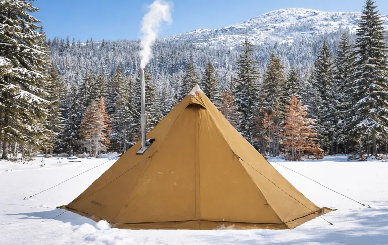 Een tent met rook, omgeven door besneeuwde bomen en bergen.