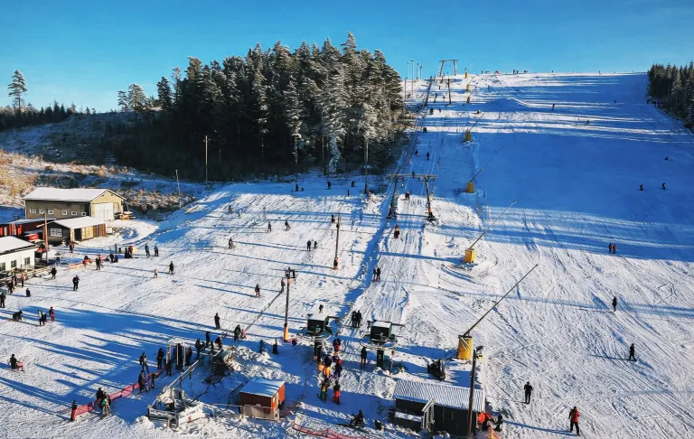 Skidområde med människor, liftar och snötäckta backar under klarblå himmel.